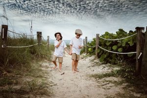 Two people walking along sandy beach path under dramatic cloudy sky.