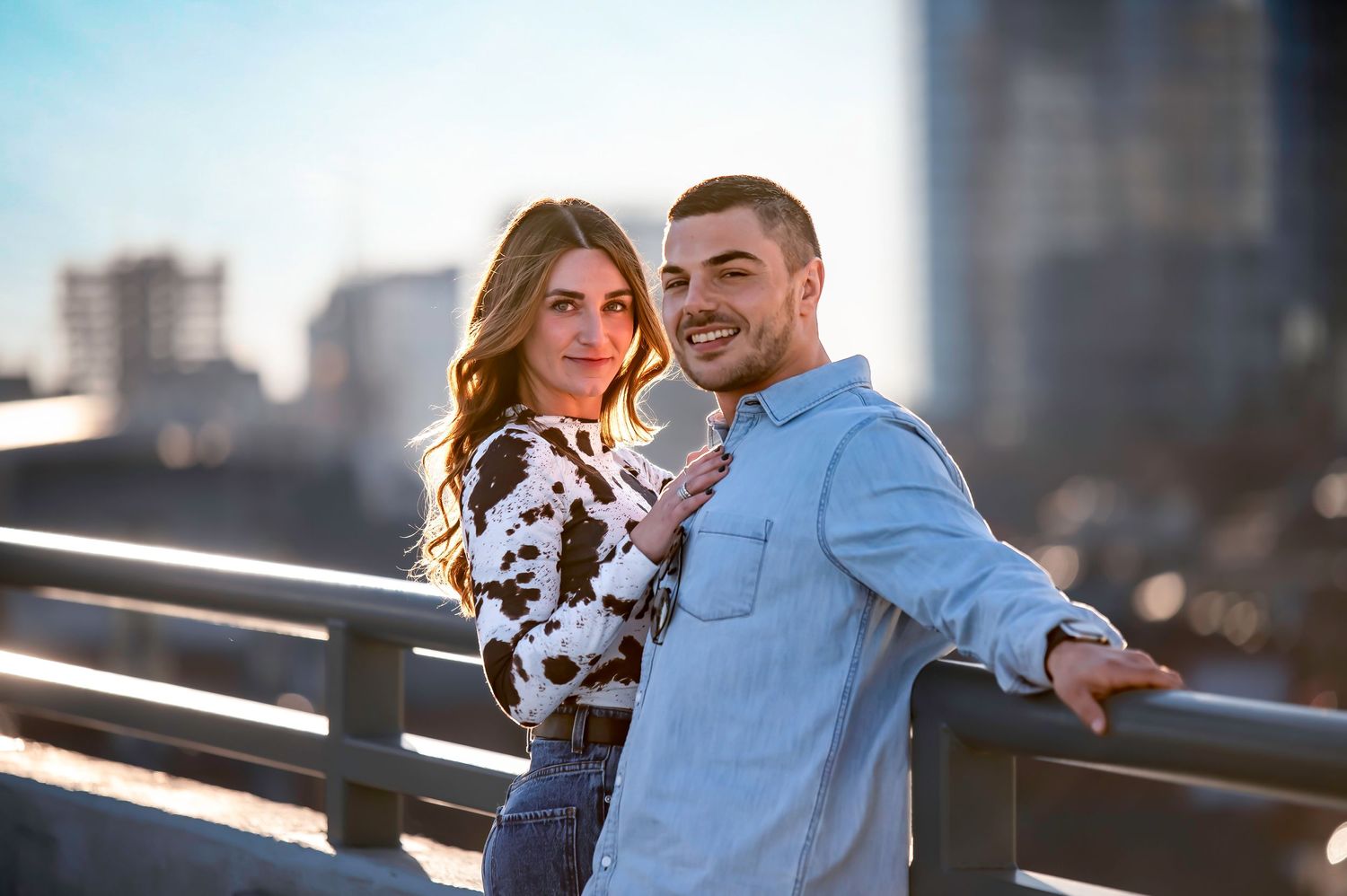 Stylish couple poses on urban rooftop with cityscape backdrop.