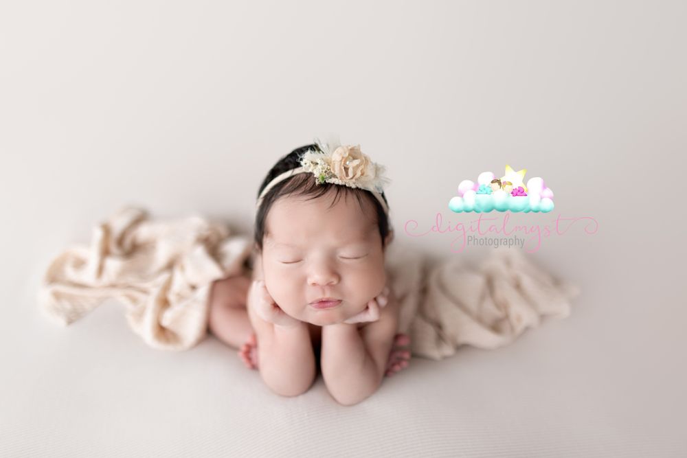 Newborn baby in crown pose on light beige background with delicate fabric.