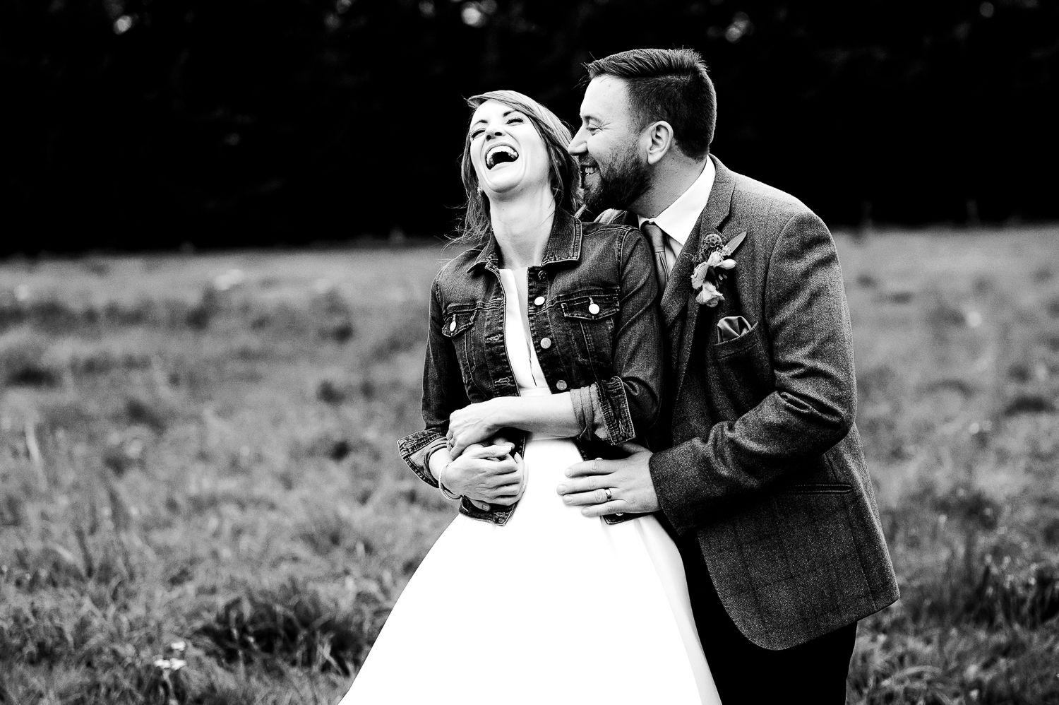 Black and white wedding photo of couple sharing joyful moment outdoors.