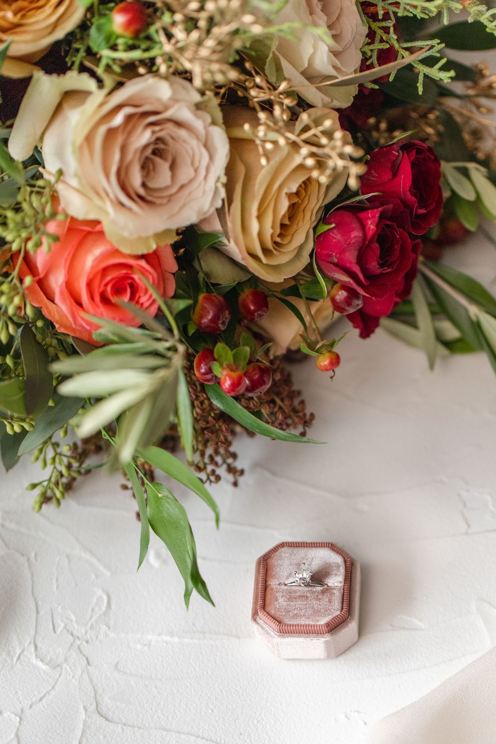 Wedding details with pink velvet ring box and romantic floral arrangement.