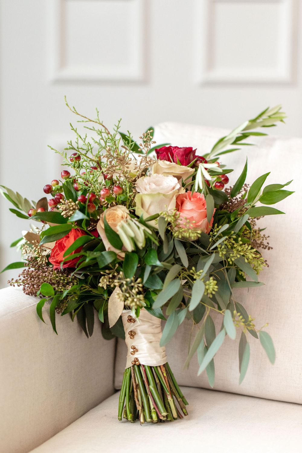 Elegant wedding bouquet with roses, berries and eucalyptus leaves on white couch.