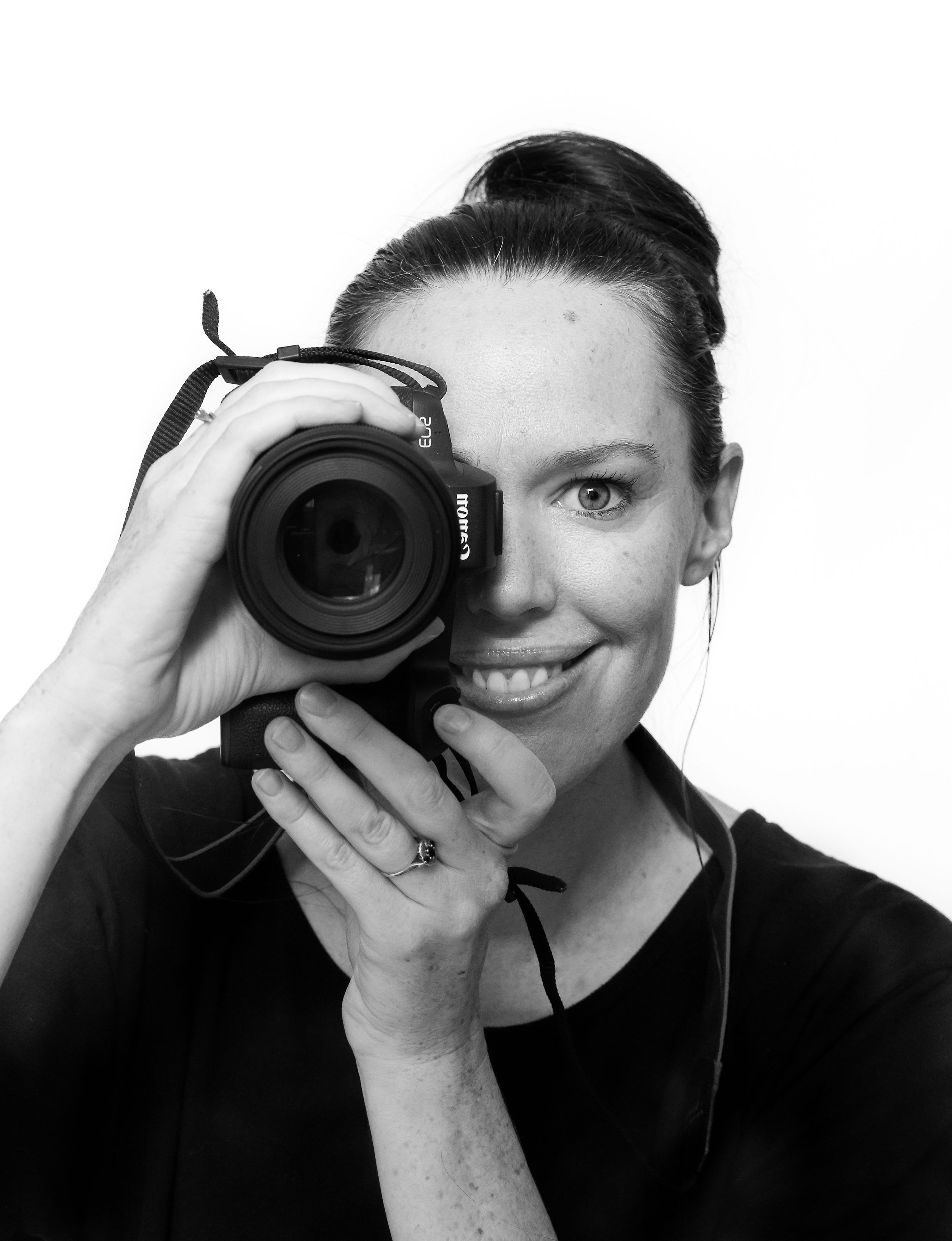 Black and White close up Image of Female Photographer smiling looking through the camera