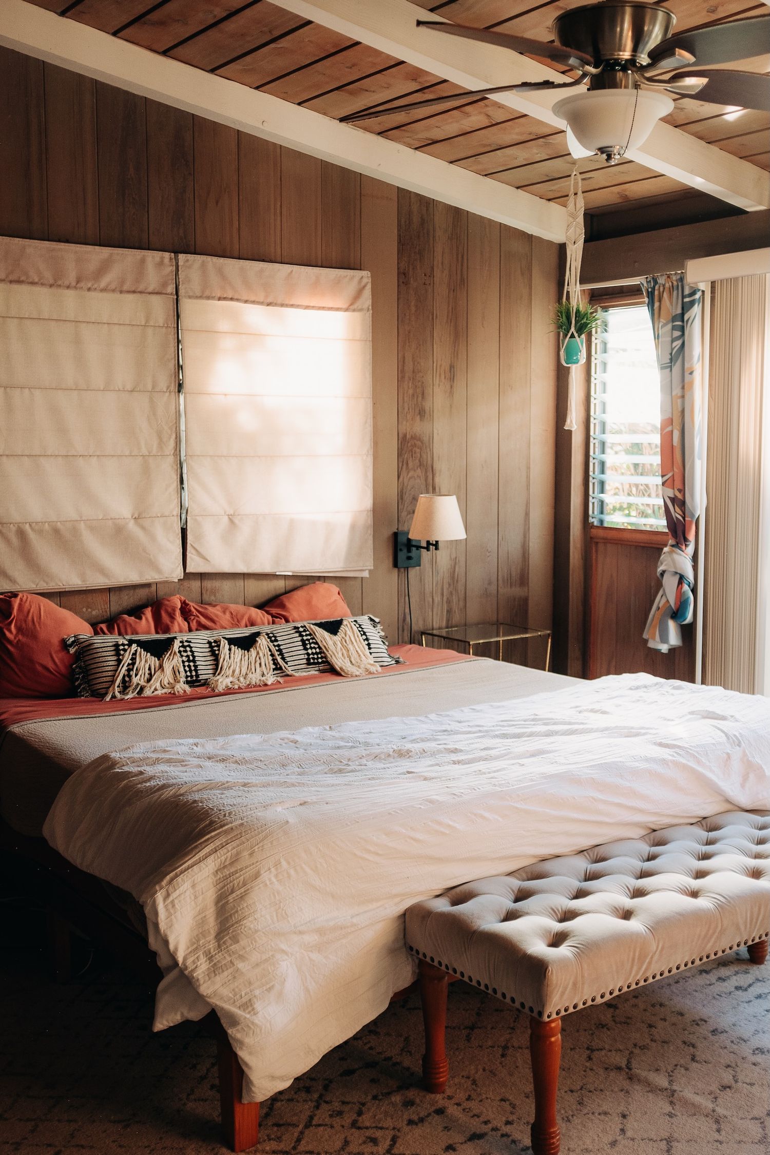 A cozy bedroom with wood paneled walls, white bedding, and a tufted bench.