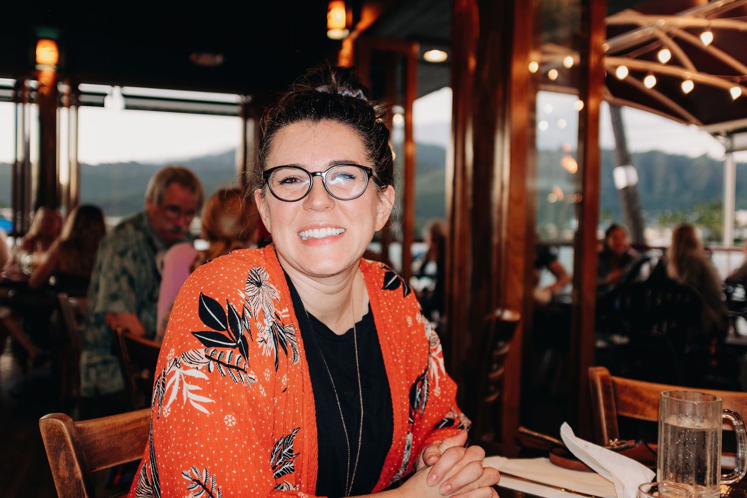 A diner setting with a customer wearing an orange patterned top and glasses seated at a table.