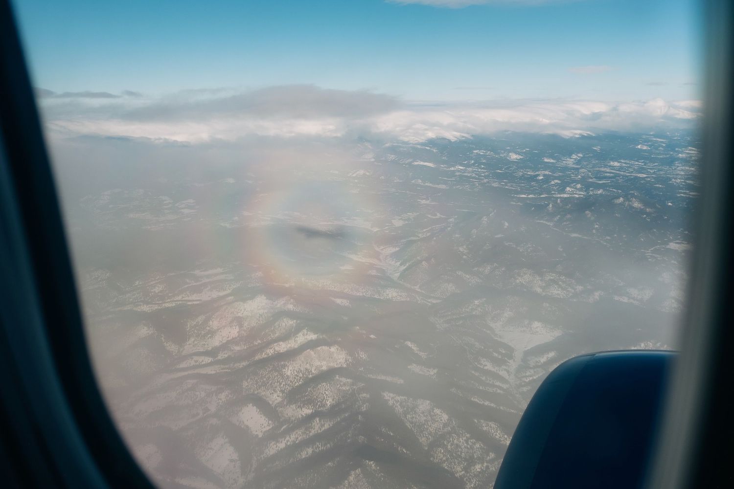 Aerial view through an airplane window showing mountains and clouds below.