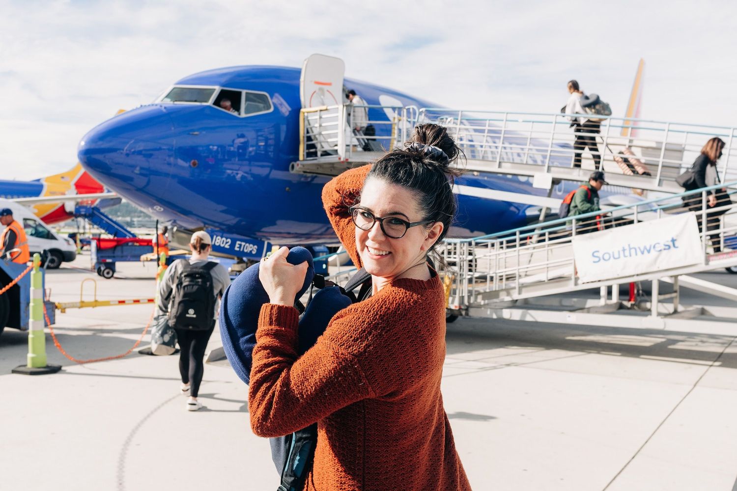 A candid shot of someone in an orange sweater standing near a large commercial aircraft.