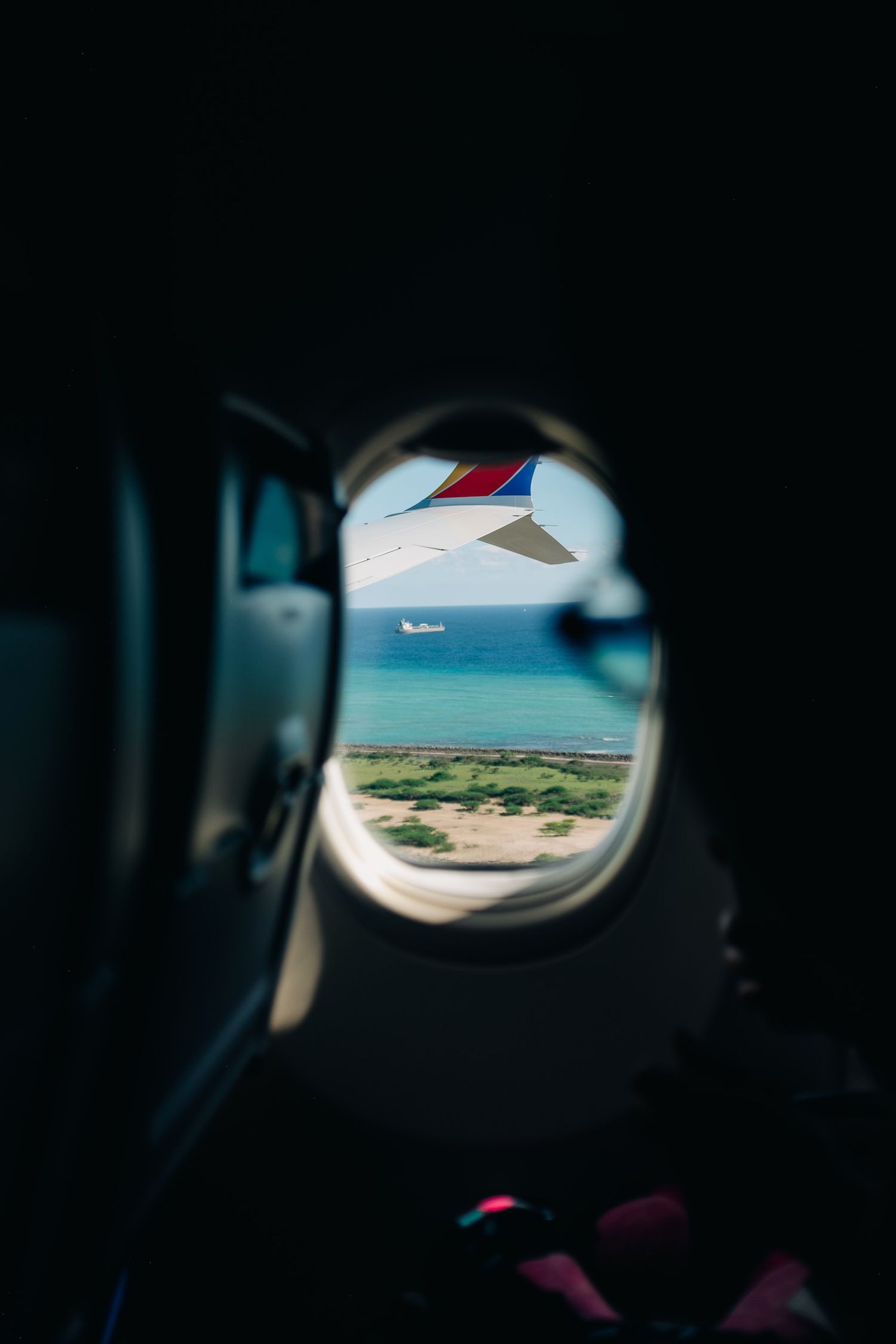 View of tropical waters and coastline through an airplane window showing the wing.
