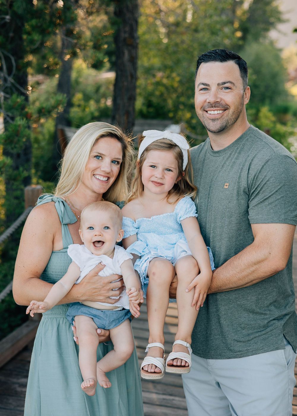Beautiful outdoor family portrait of four people on a wooden deck surrounded by trees.