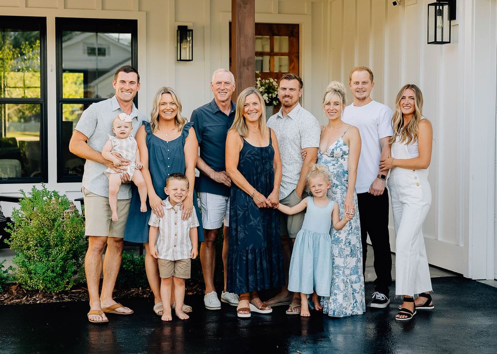 Group portrait of extended family members gathered on front porch of white farmhouse.