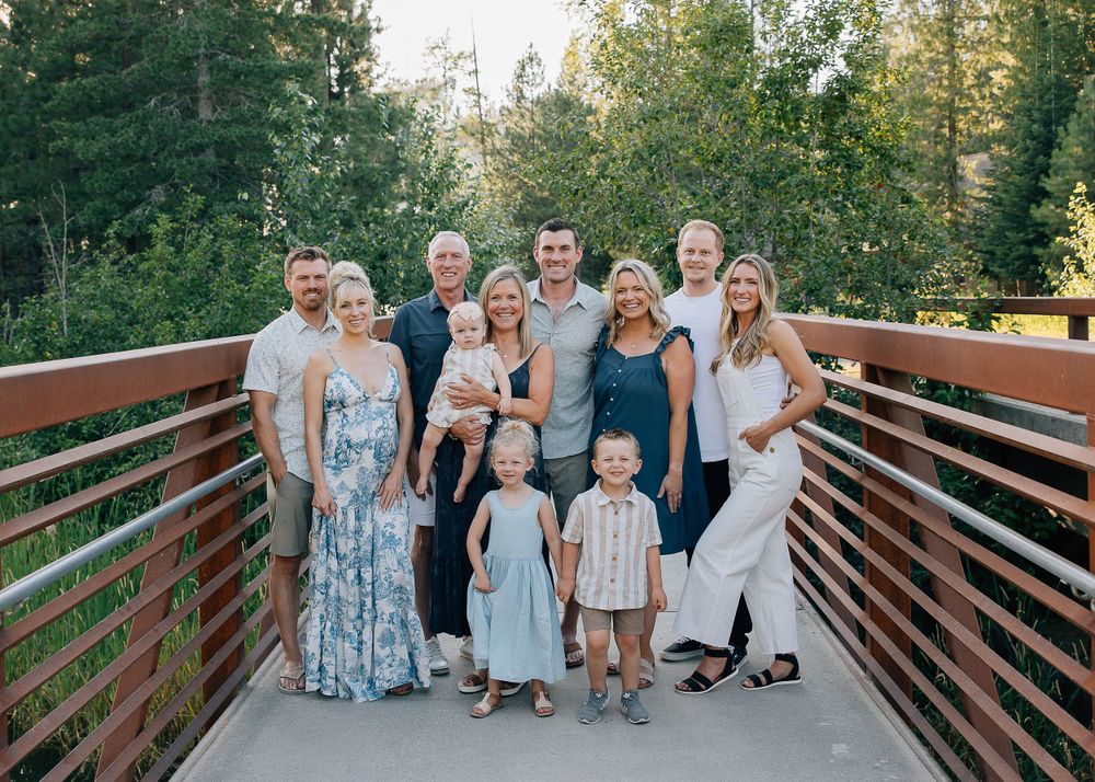 Multi-generational family portrait on wooden bridge with forest background.
