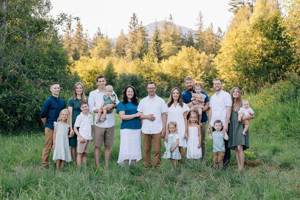 Large family group in coordinated white and neutral outfits poses together in sunny meadow.