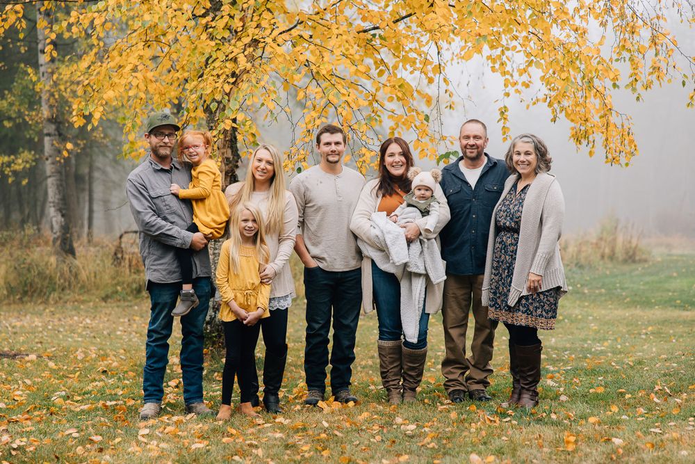Group portrait of extended family in warm autumn setting with golden leaves overhead.