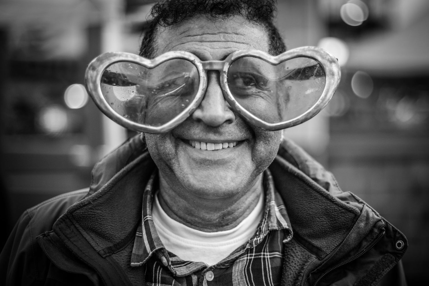 Black & White Portrait of a Stranger of a man wearing oversized heart shaped sunglasses with a slight smile on his face.