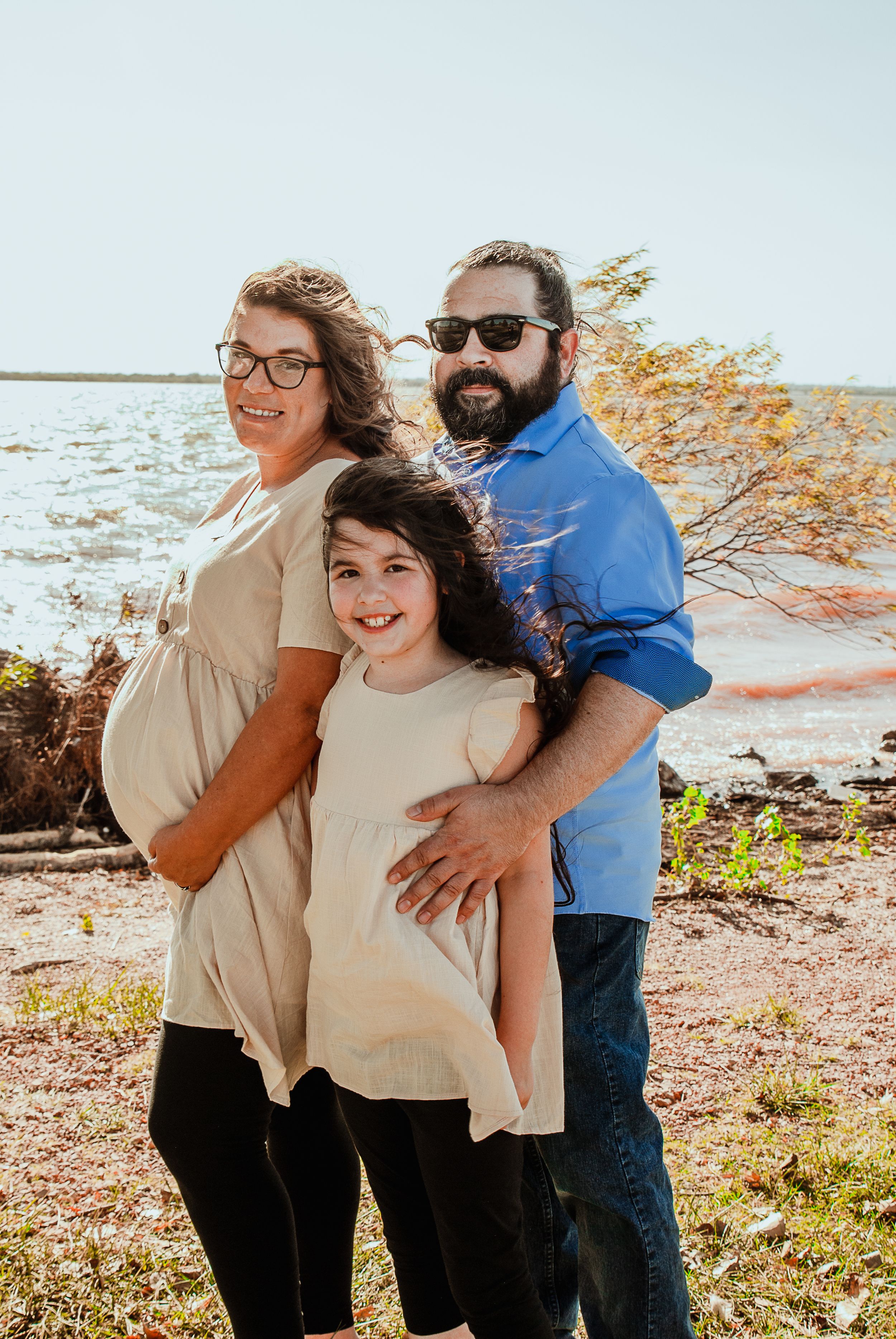 a family photo with a pregnant woman holding her belly, the father standing behind and the two of them hugging their daughter in front of a