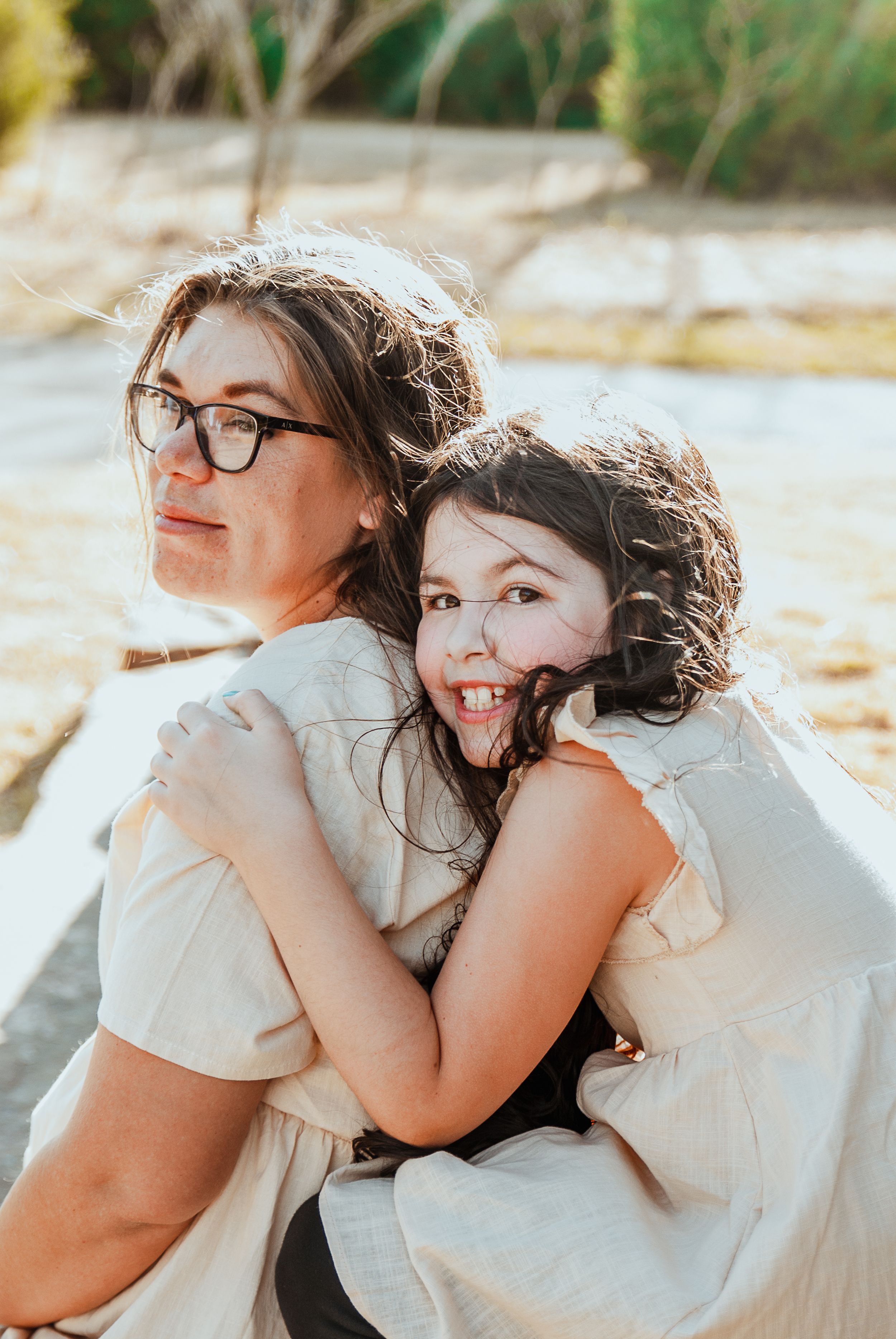 a family photo with a daughter hugging her mother from behind while seated on a bench