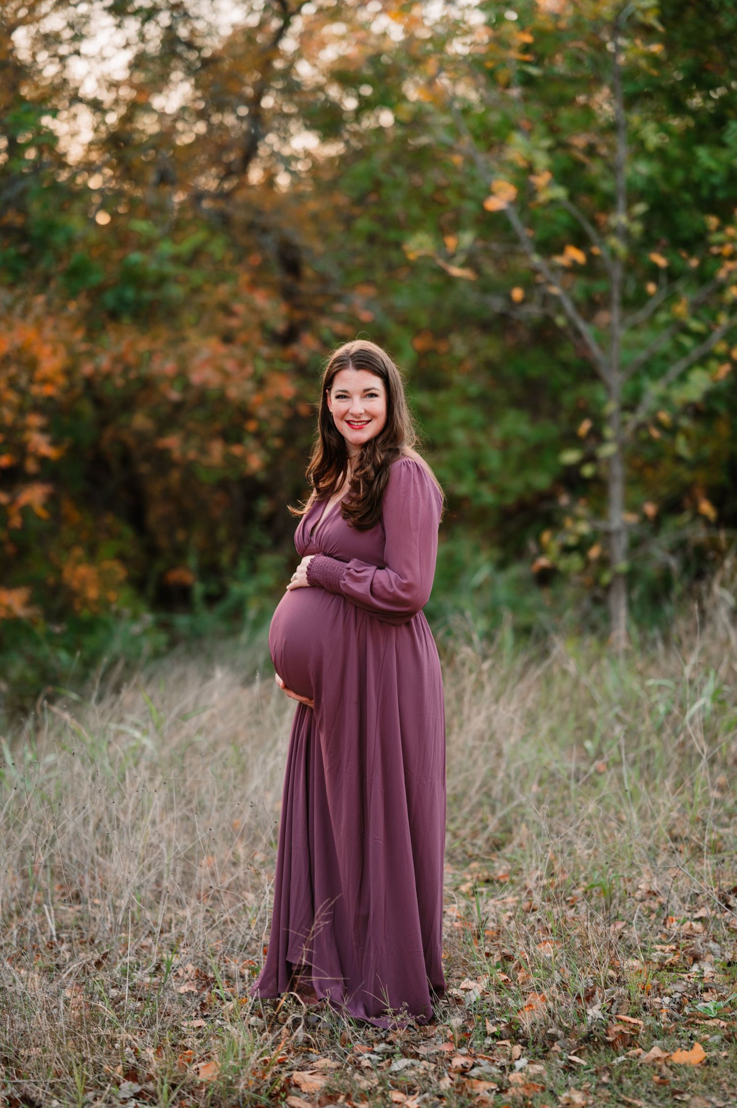 Mother poses holding her bump in deep purple gown for her richardson outdoor blue hour maternity photo session