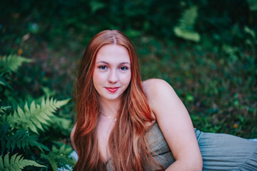An artistic outdoor portrait featuring long auburn hair and a natural forest backdrop.