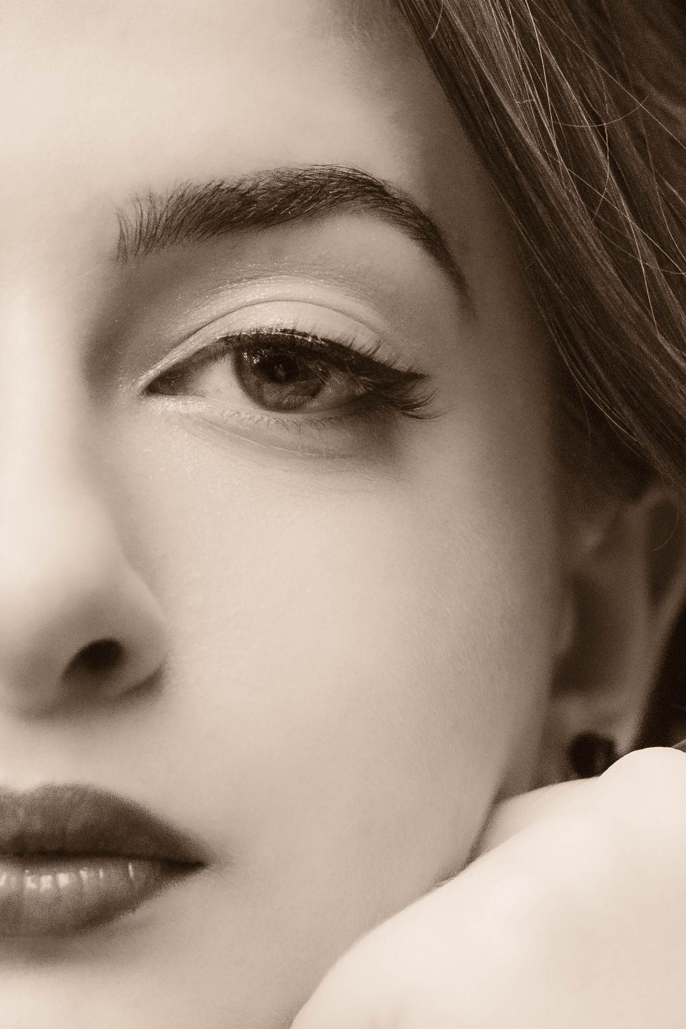 Close-up beauty portrait showing detailed eye makeup and brow in sepia tones.