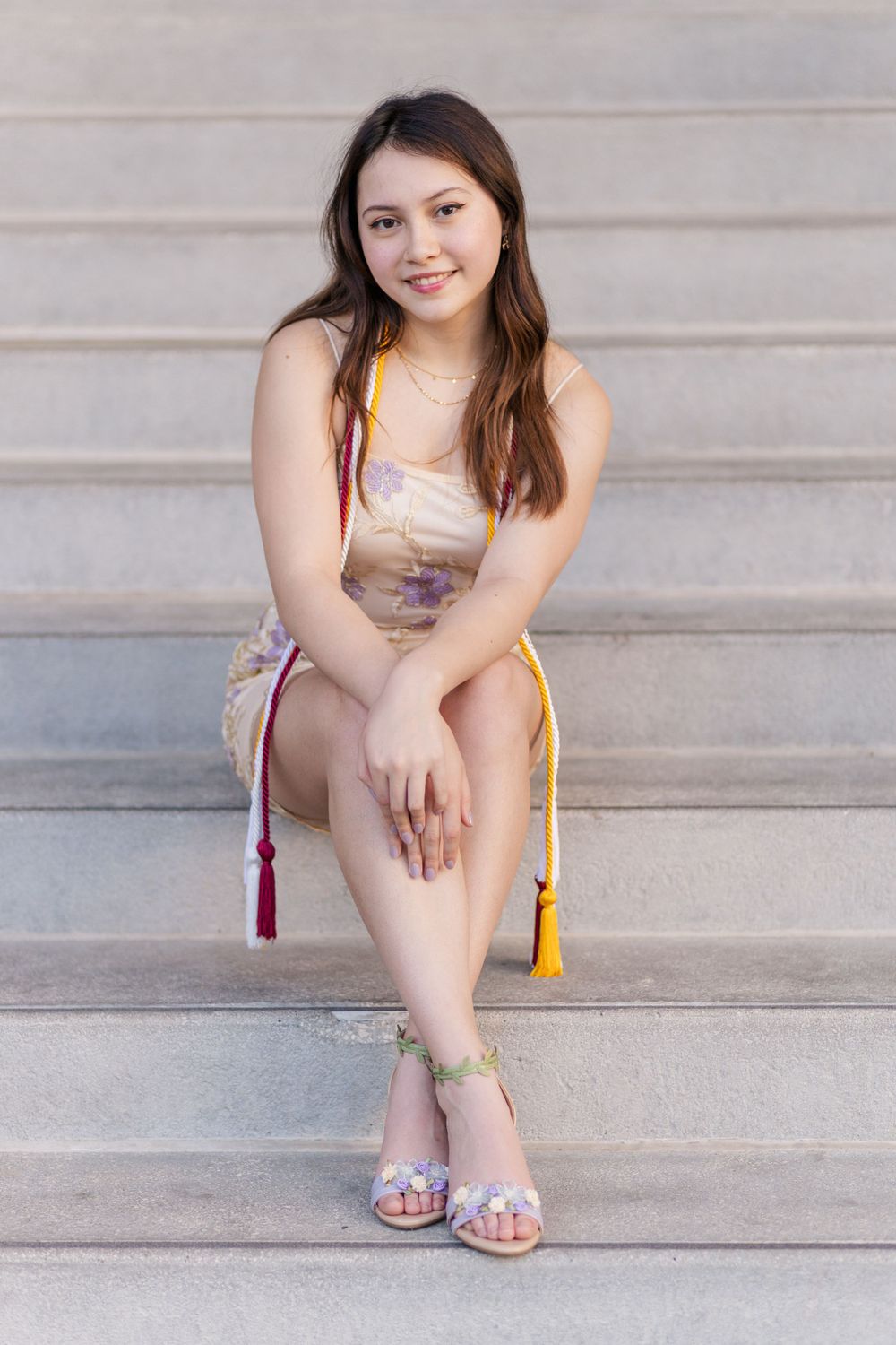Student in sparkly dress sits casually on concrete steps with decorative tassels.