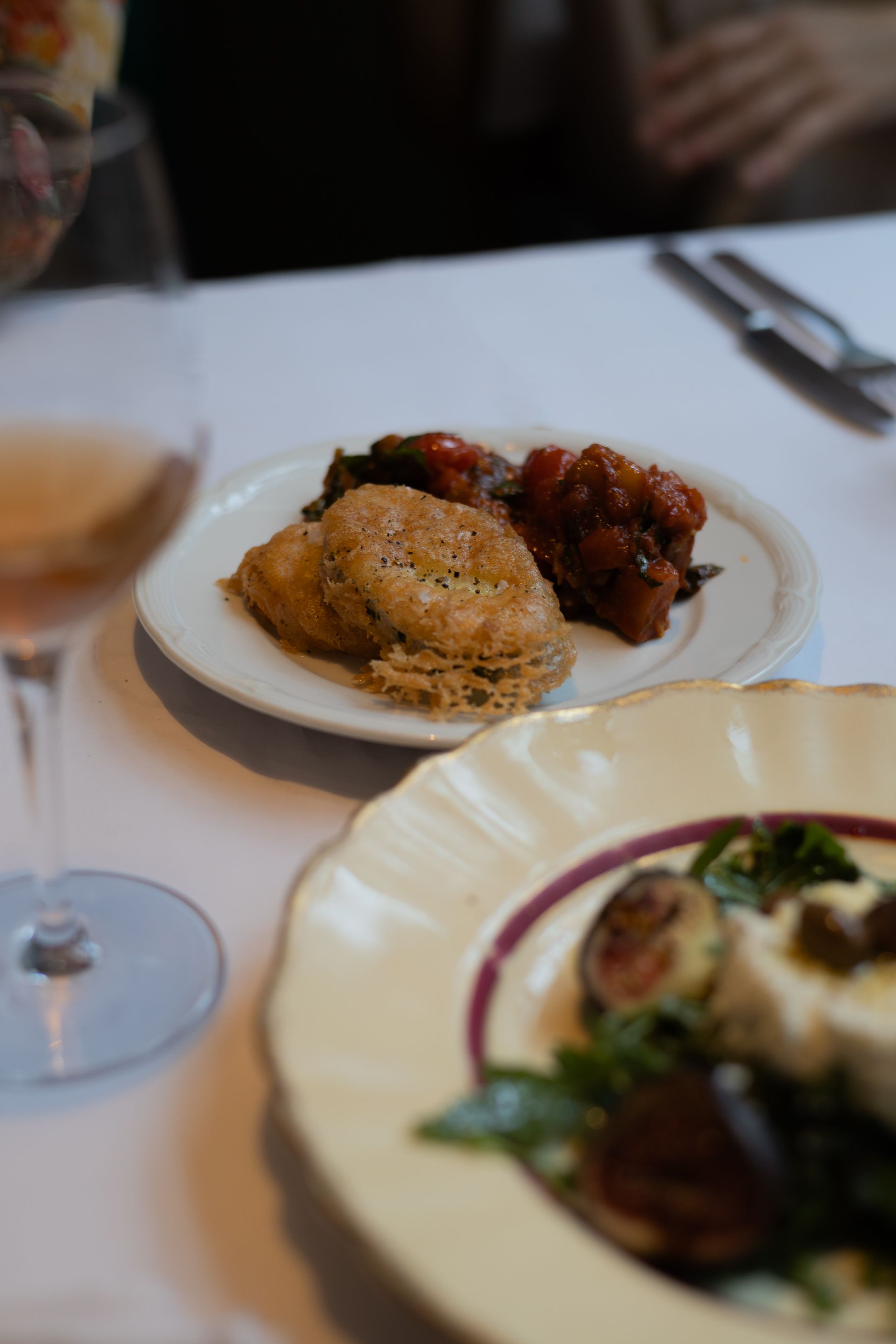 Fine dining table setting with biscuits, meat dish and wine glass on crisp white linen.