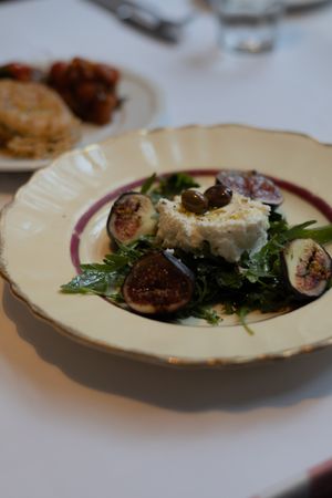 A plate of grilled figs with cheese and greens served on a cream-colored dish with burgundy trim.