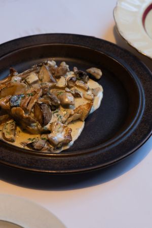 A creamy mushroom dish served in a black ceramic plate with fresh herbs.