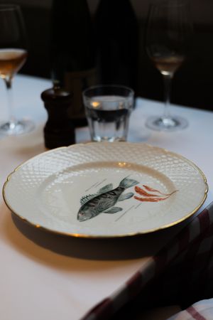 A decorative plate with a painted fish design and gold trim on a white tablecloth.