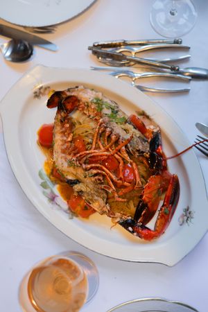 A beautifully plated whole lobster dish with cherry tomatoes and herbs on a white oval platter.