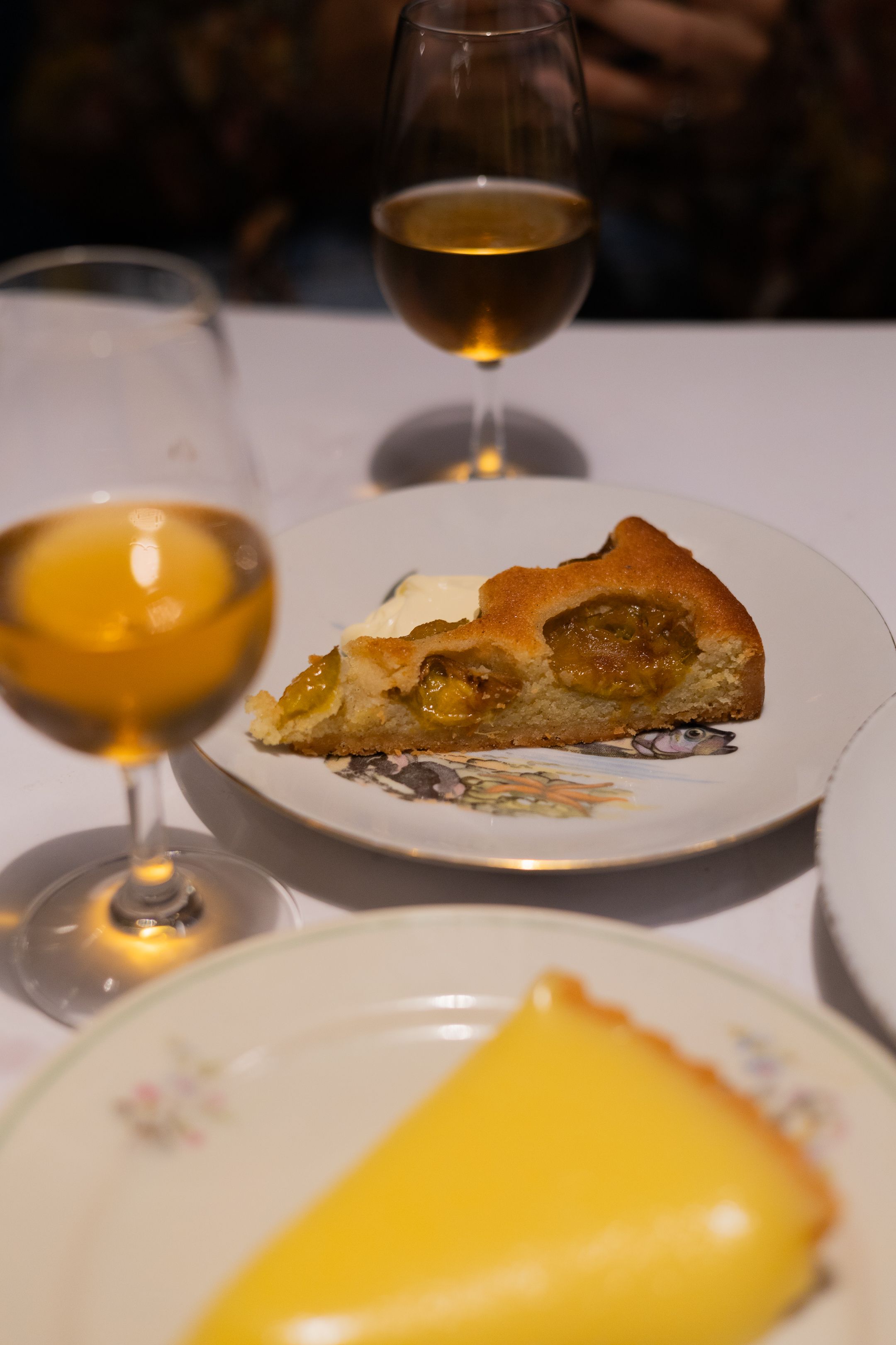 Two dessert plates with pastry and lemon tart served alongside golden wine glasses.