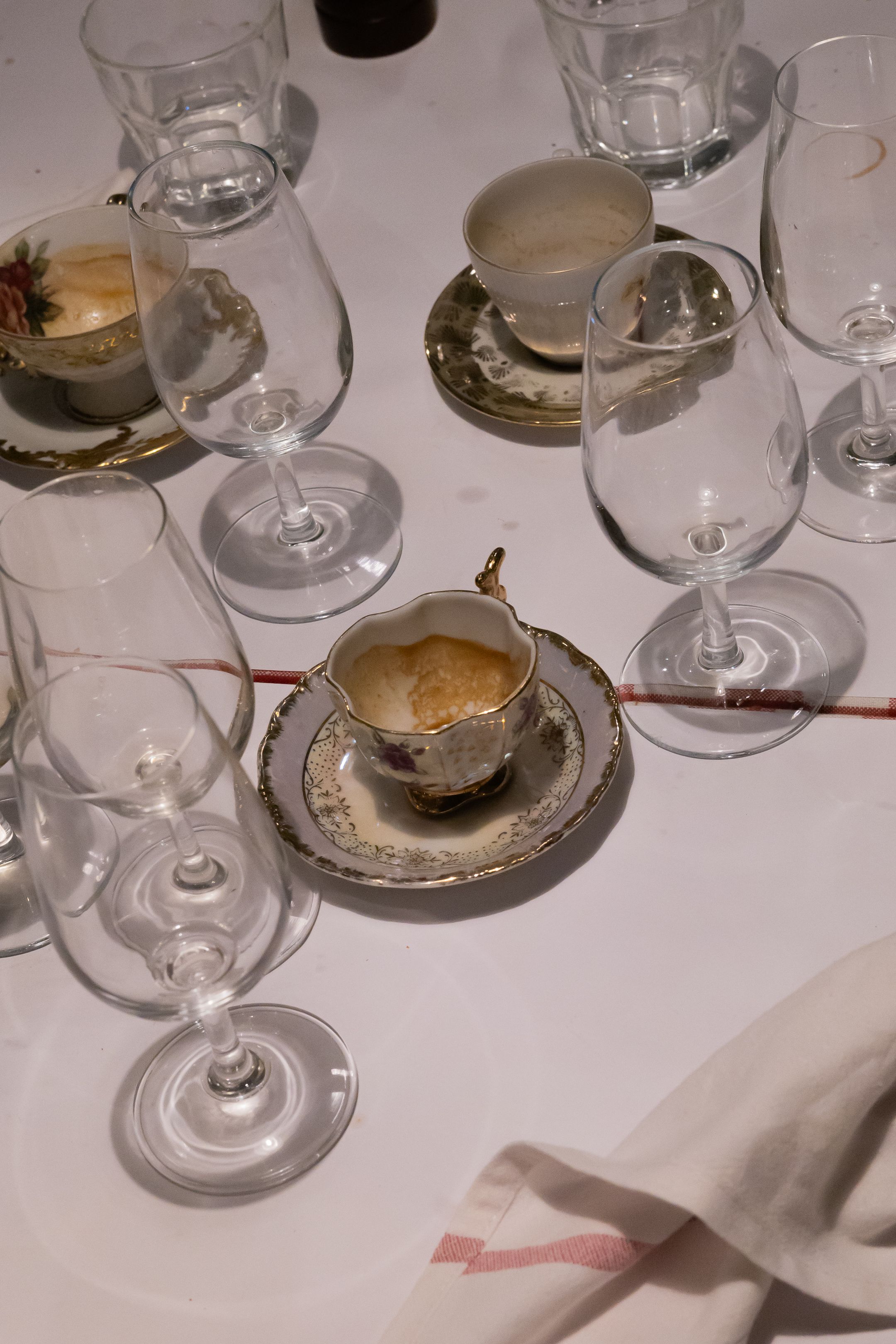 Elegant table setting with vintage teacups and wine glasses on white tablecloth.