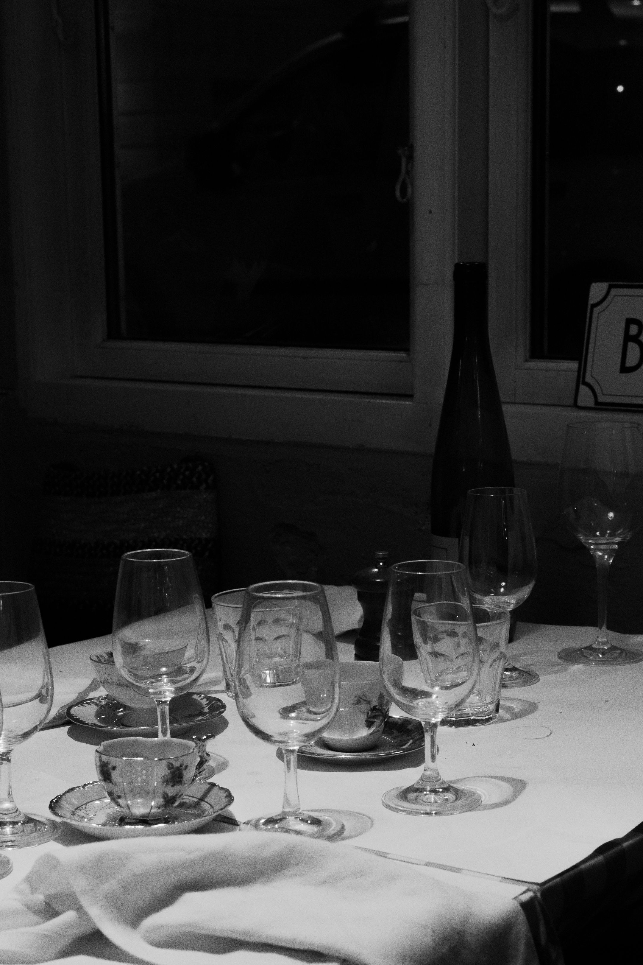 Black and white photo of formal dining setup with wine glasses and teacups.