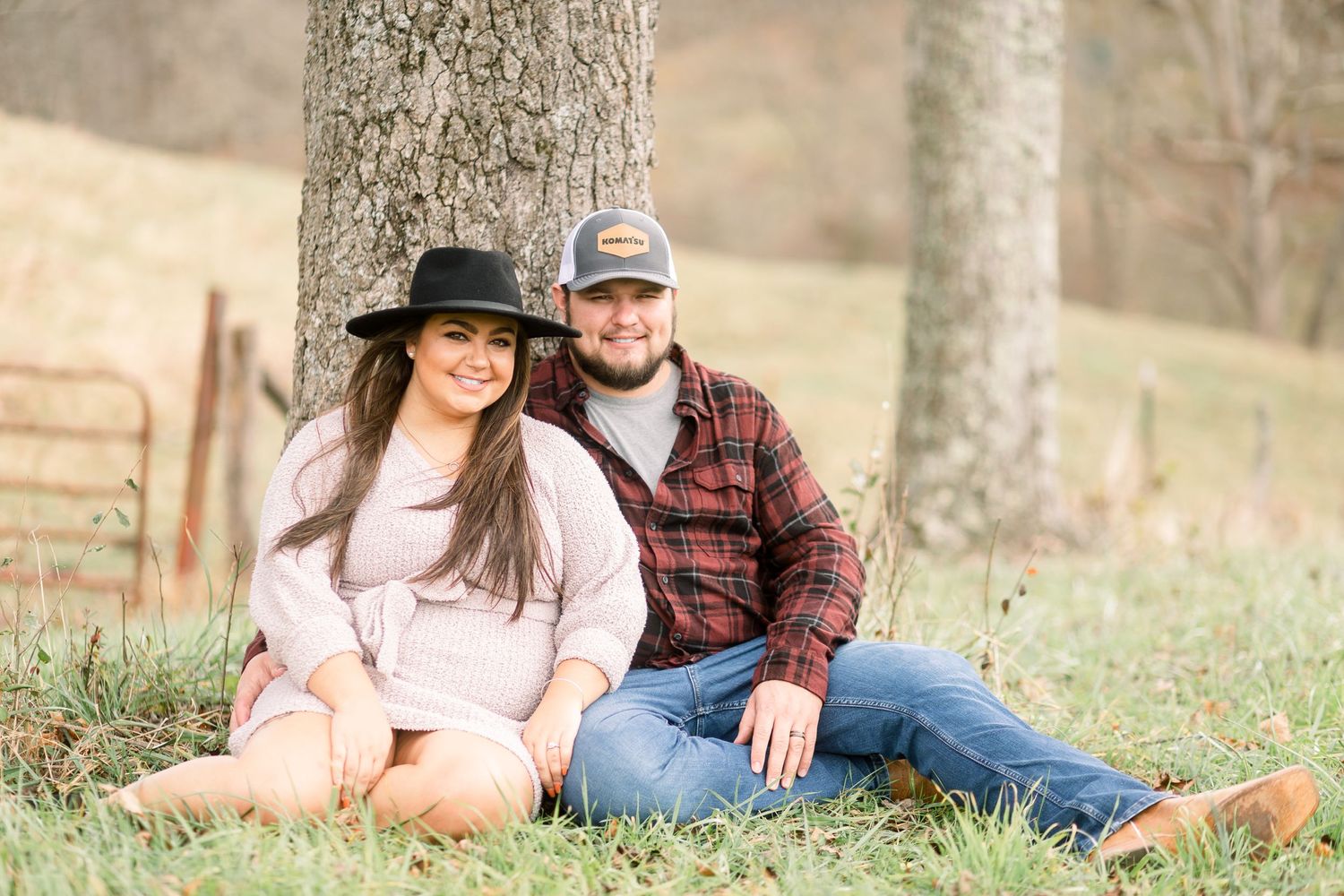 Couple relaxes on grass near trees during an outdoor photo session.
