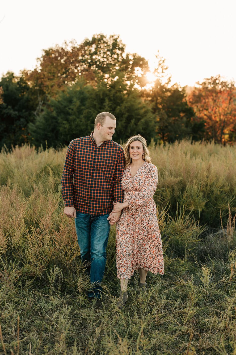 Couple walking through autumn field during sunset portrait session.