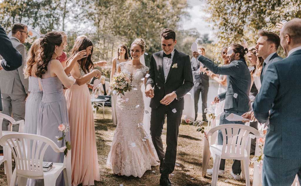 Wedding couple walking down aisle while guests throw confetti in outdoor garden celebration.