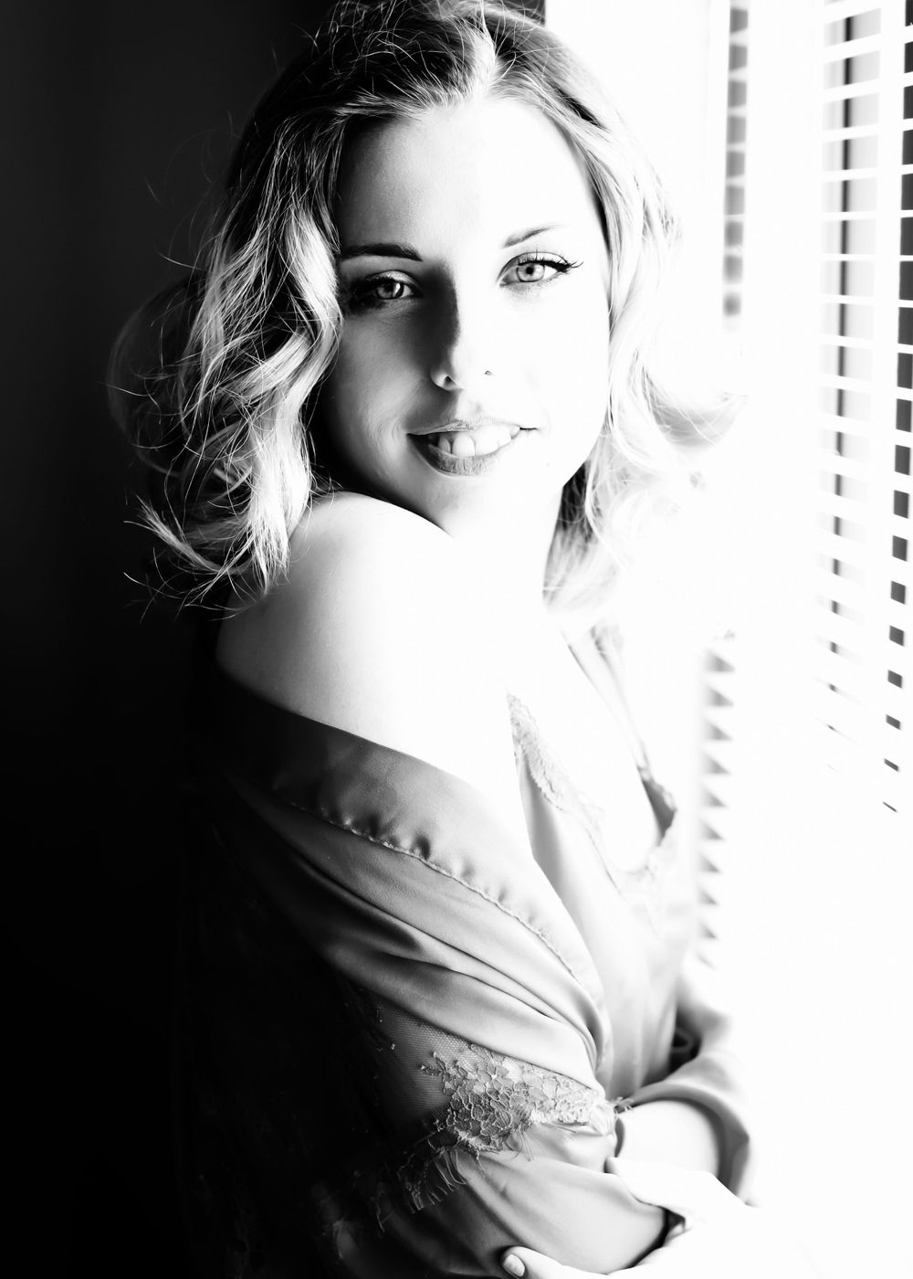 blond woman in mans shirt posing in front of window