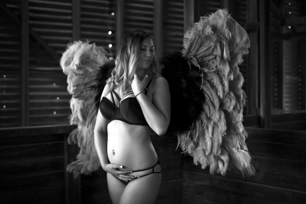 long haired woman in lingerie and feather wings posing for camera in old shed