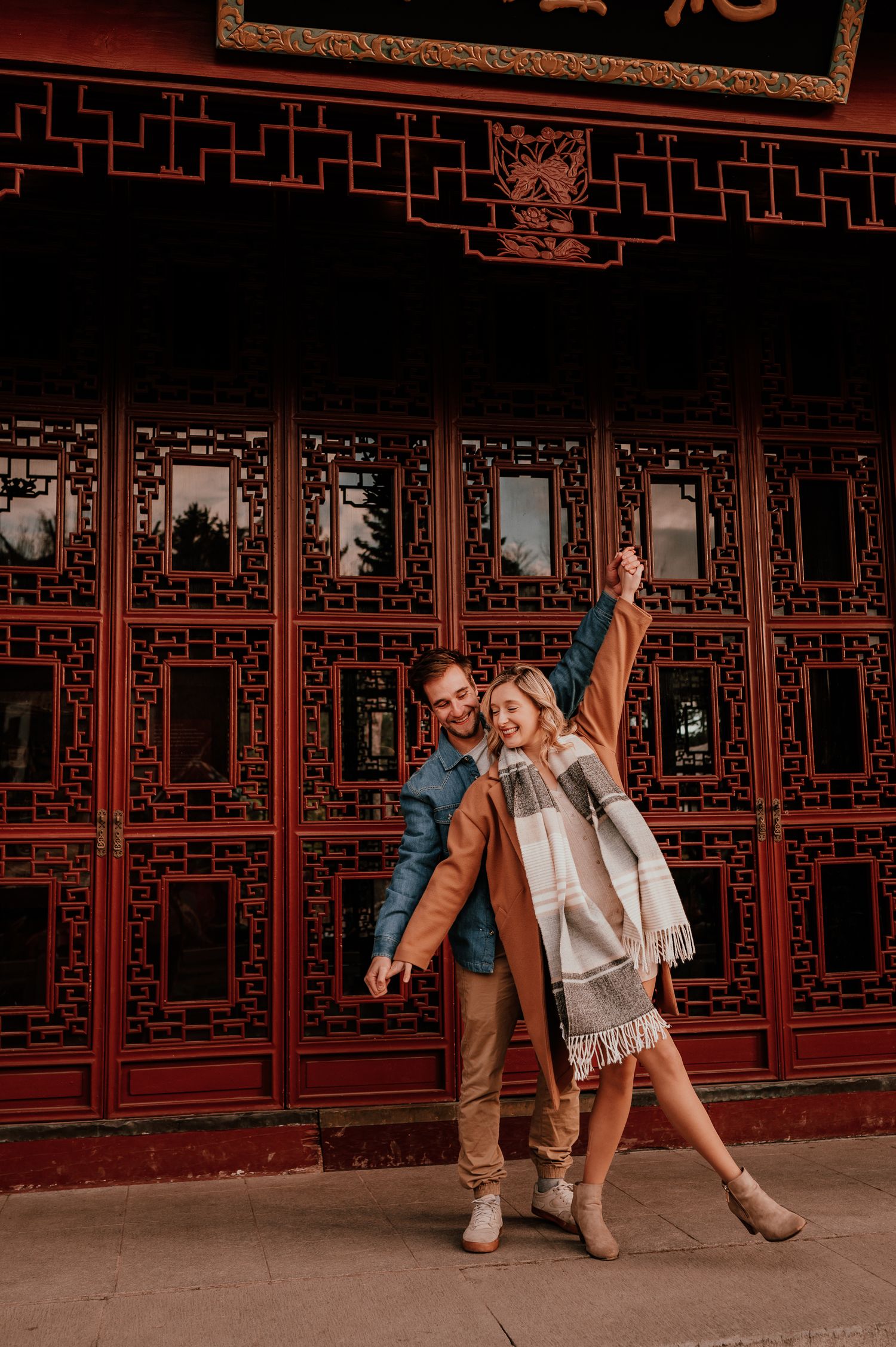 Playful couple poses in front of ornate red Chinese architectural details.