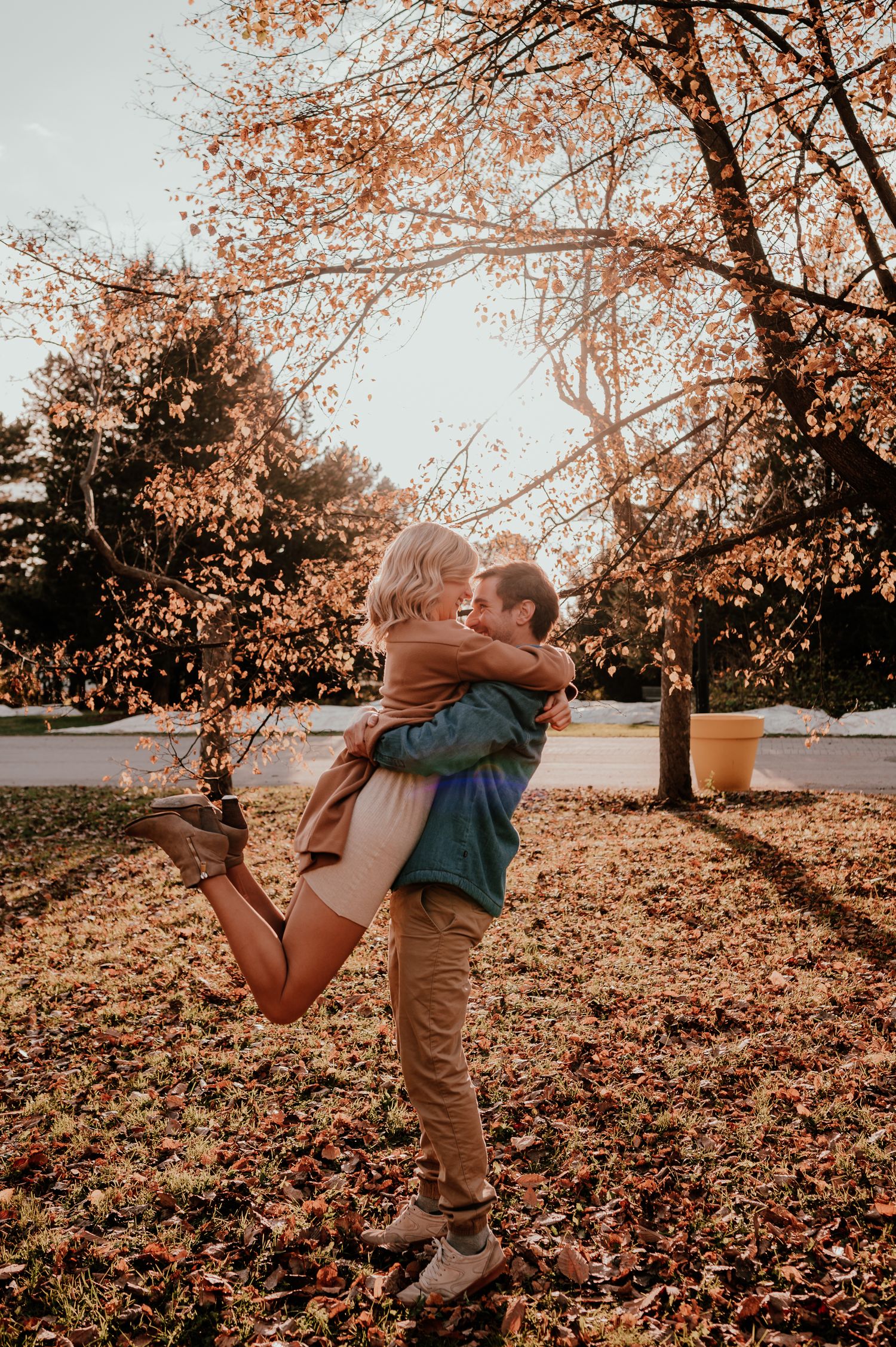 Romantic lifestyle photo of couple embracing under fall trees with golden sunlight.