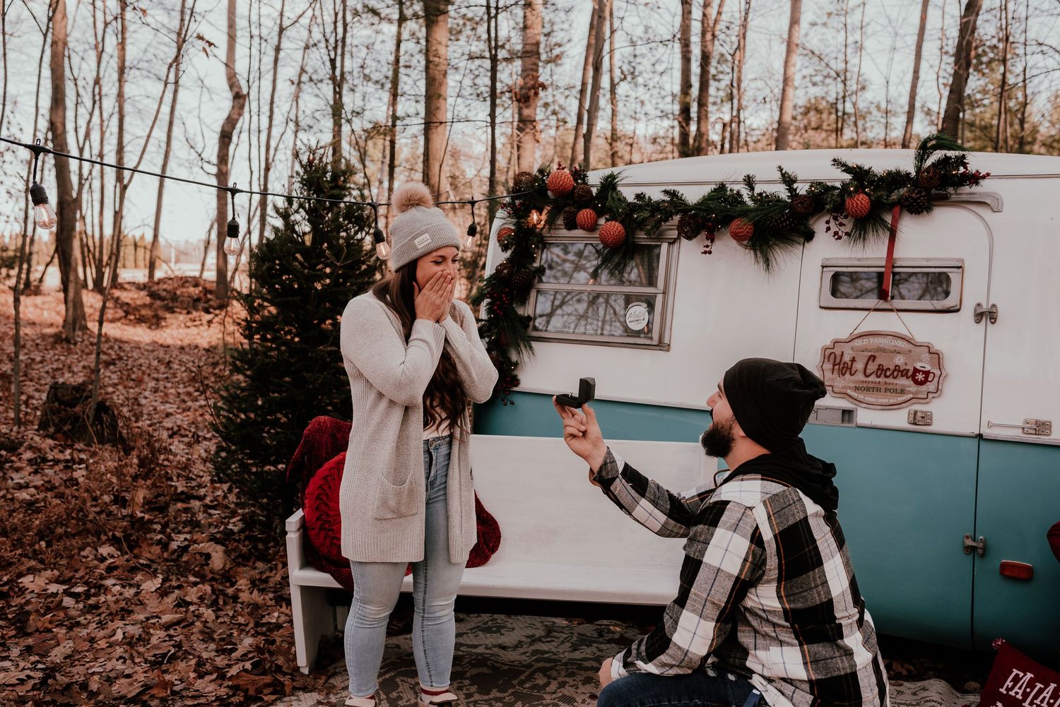 Romantic winter proposal scene in front of vintage blue and white camper van with holiday decorations.