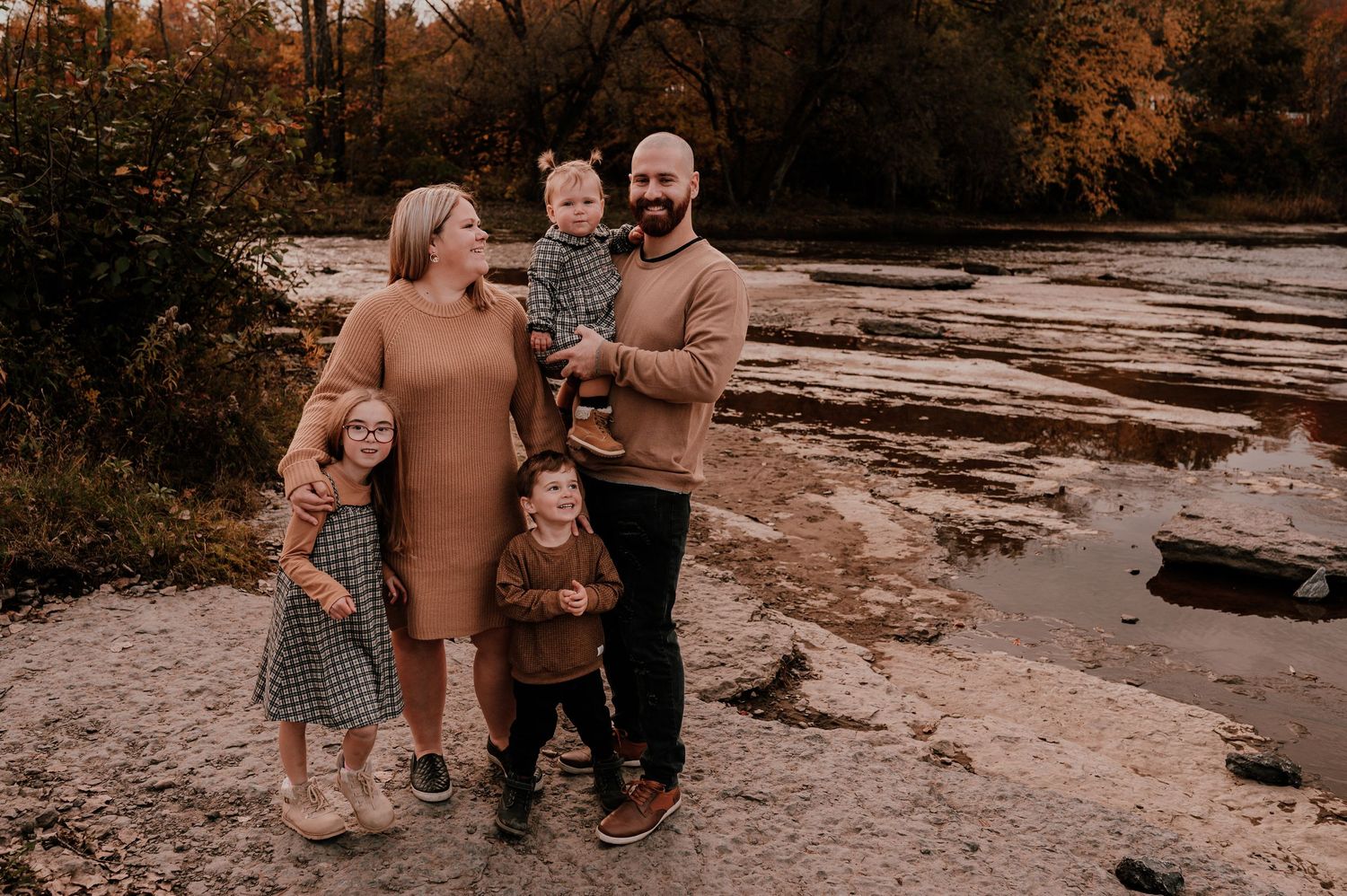 Family in coordinating tan outfits poses together on rocky riverbank.