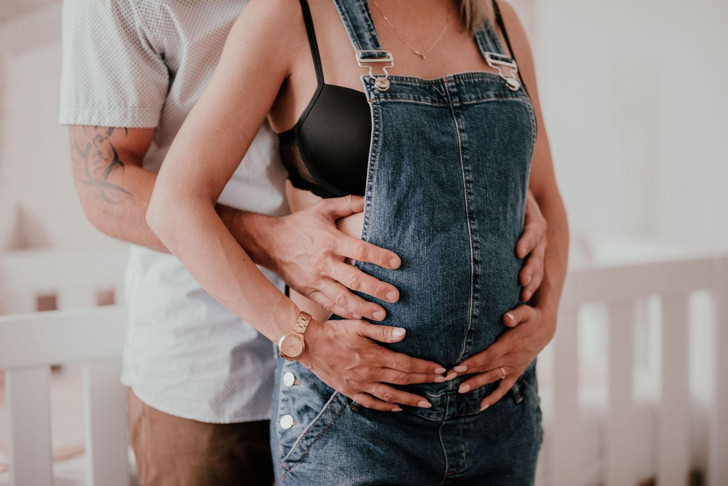 A couple embraces while showing off their baby bump in denim overalls.