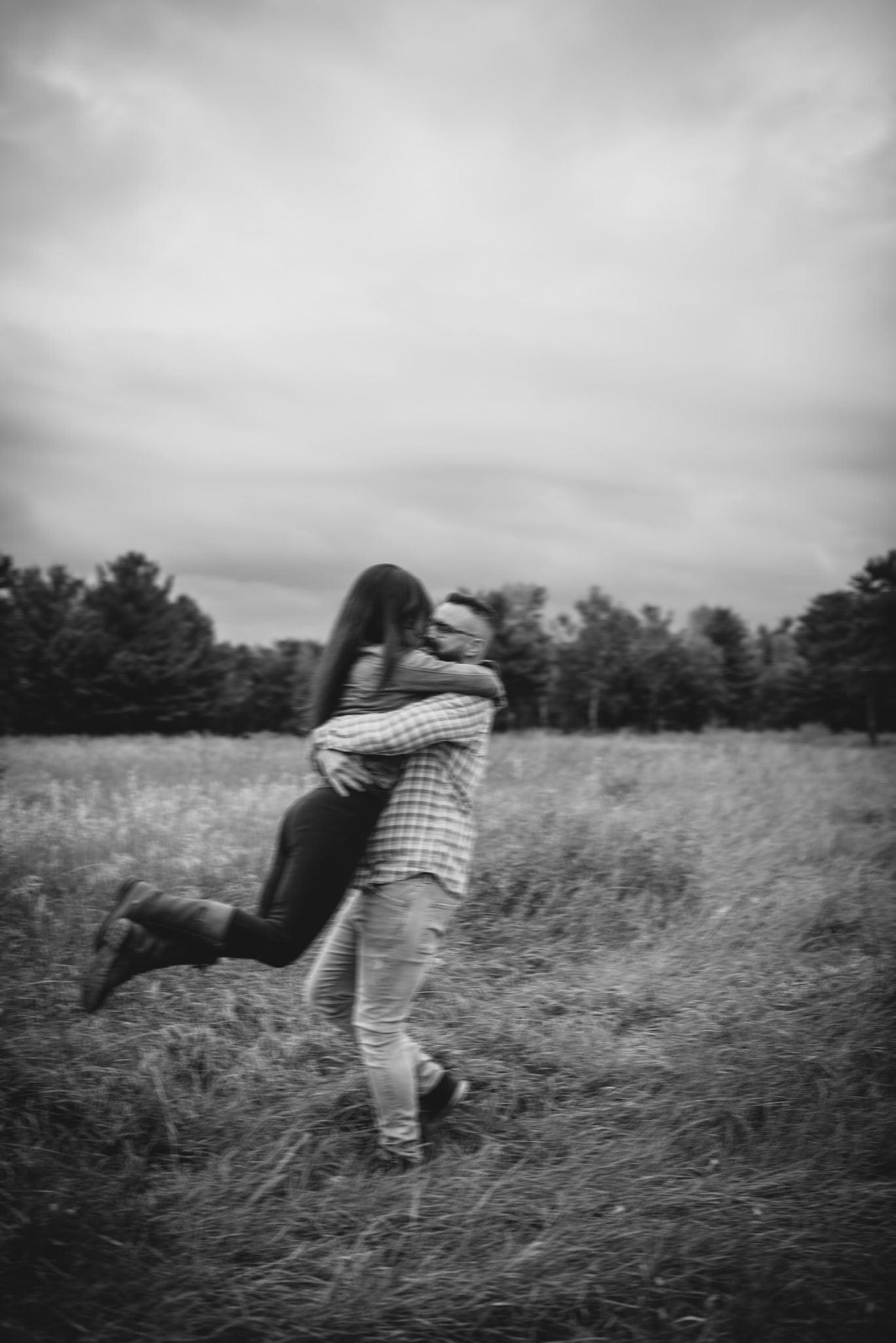 A playful couple spinning in an autumn field captured in black and white.