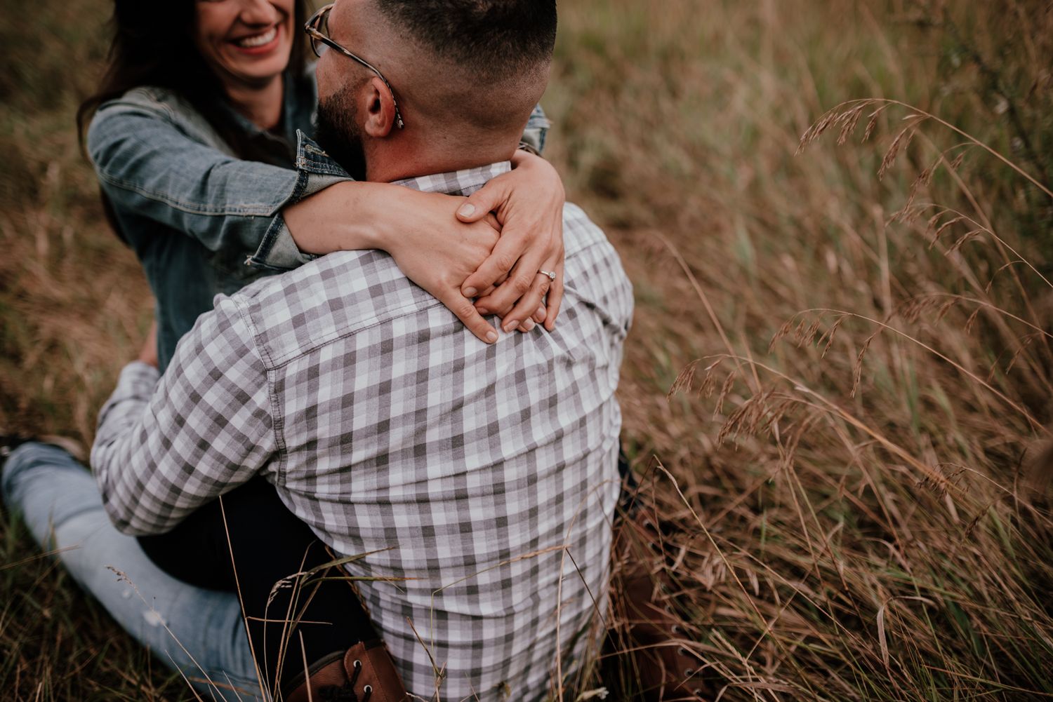 A couple embraces in tall grass during a romantic outdoor photoshoot.