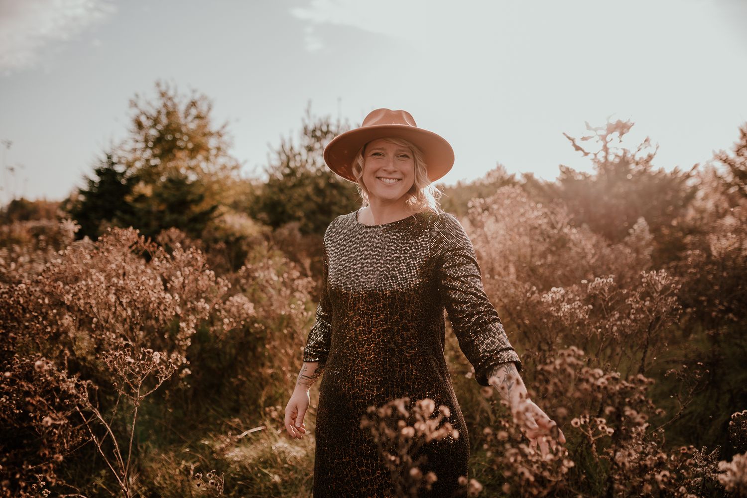 A person in a hat poses joyfully among autumn foliage at golden hour.