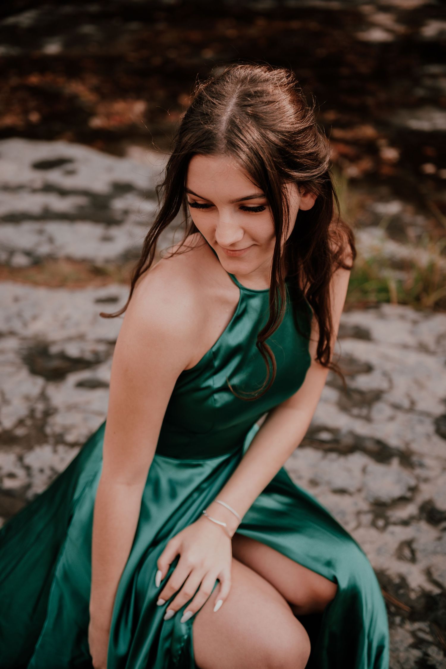 A woman in an emerald green formal dress poses on rocky terrain.