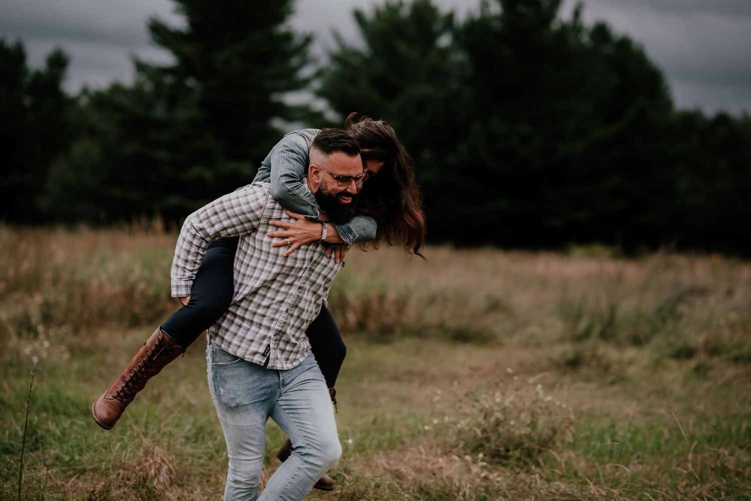 A couple plays and laughs together in a field during sunset.