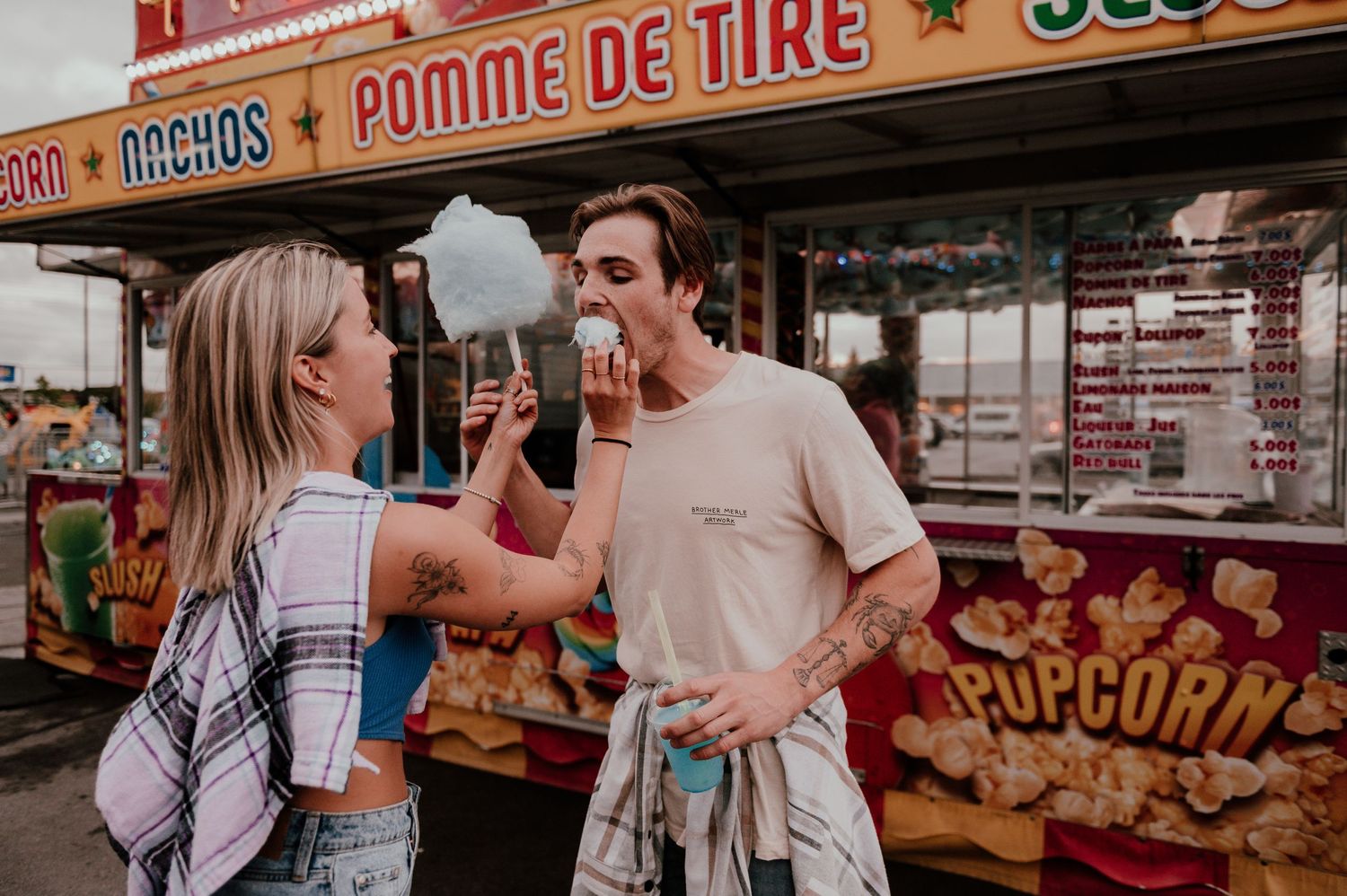 Couple sharing cotton candy at carnival food stand.