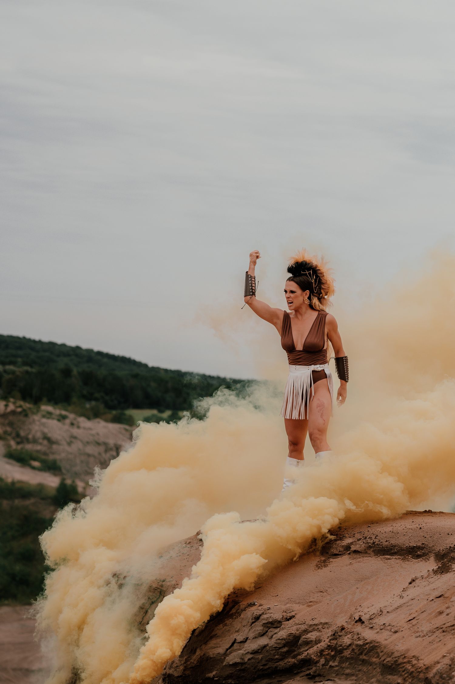 Figure stands triumphantly on cliff edge surrounded by dramatic yellow smoke bombs.