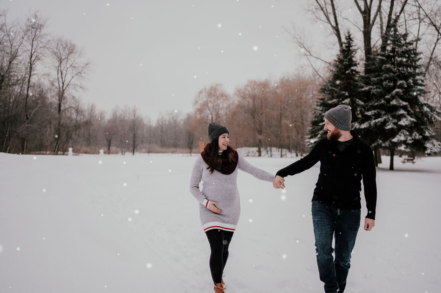 Couple holding hands while walking through snowy winter landscape.